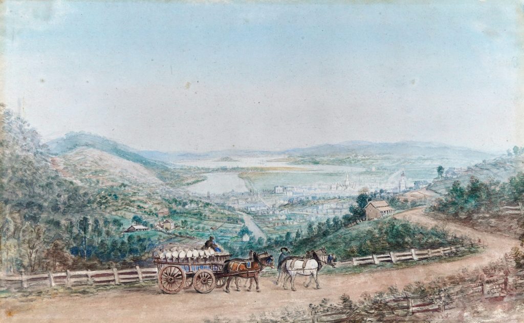 A man driving a loaded cart with four horses, on a road above Launceston looking out over the town of Launceston and the Tamar River.