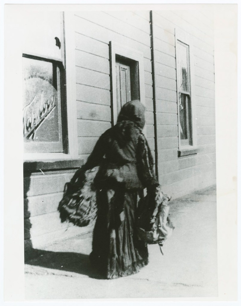 Mary Patches, an elderly hawker known for her patchwork skirt, walking past the Park Hotel in early 1900s Tasmania.