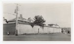 Black and white view of the Old Launceston Gaol from Bathurst Street, showing high brick walls, a pedestrian passing and early twentieth century rooftops.